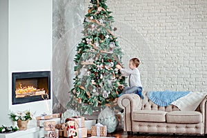 Cute boy decorates the Christmas tree with Christmas balls, gifts under the Christmas tree