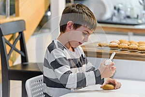 Cute boy decorating holiday gingerbread cookies at home kitchen