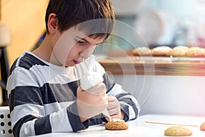 Cute boy decorating holiday gingerbread cookies at home kitchen