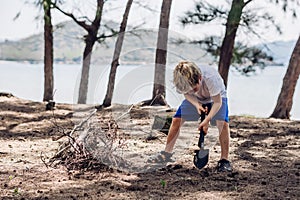 Cute boy digging soil in forest near sea beach. Family natural education skills. Travelling together. Learning camping