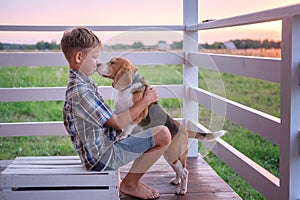 Cute boy and dog Beagle sitting hugging on the veranda