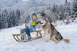 Cute boy with dog enjoying a sleigh ride. Child sledding, riding a sledge play outdoors in snow in winter park. Outdoor