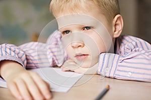 Cute boy doing his homework and looking tired.