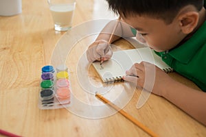 Cute boy doing homework, coloring pages, writing and painting. Children paint. Kids draw. Preschooler with books at home.