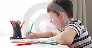 Cute boy drawing on a piece of paper with color pencils at home or classroom