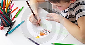 Cute boy drawing on a piece of paper with color pencils at home or classroom