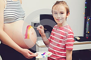 Cute boy drawing rainbow on pregnant belly his mother. Baby birth expecting time and belly painting