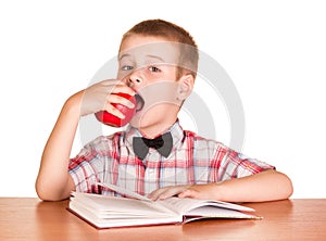 Cute boy eating apple while sitting at table isolated.