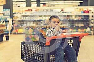 Cute boy eating a bun or pita bread in a supermarket in the cart. Hungry child in the store. toned