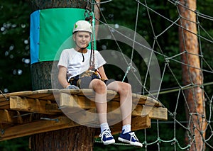 Cute boy enjoying activity in climbing adventure park at sunny summer day. Kid climbing in rope playground structure.