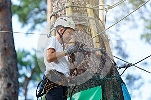 Cute boy enjoying activity in climbing adventure park at sunny summer day. Kid climbing in rope playground structure.