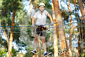 Cute boy enjoying activity in climbing adventure park at sunny summer day. Kid climbing in rope playground structure.