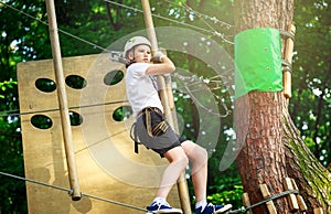 Cute boy enjoying activity in climbing adventure park at sunny summer day. Kid climbing in rope playground structure.