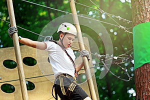 Cute boy enjoying activity in climbing adventure park at sunny summer day. Kid climbing in rope playground structure.