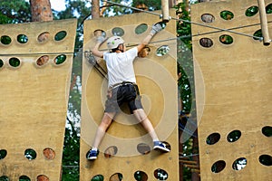 Cute boy enjoying activity in climbing adventure park at sunny summer day. Kid climbing in rope playground structure. Safe