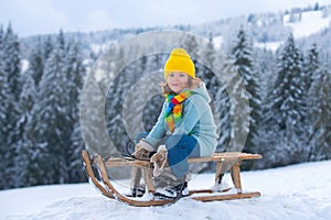 Cute boy enjoying a sleigh ride. Child sledding, riding a sledge play outdoors in snow on winter landscape. Outdoor