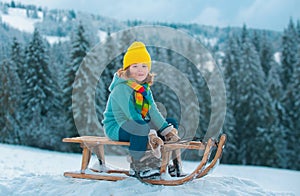 Cute boy enjoying a sleigh ride. Child sledding, riding a sledge play outdoors in snow on winter landscape. Outdoor