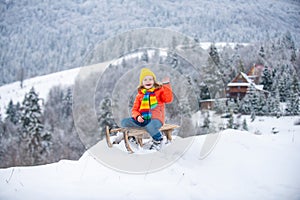 Cute boy enjoying a sleigh ride. Child sledding, riding a sledge play outdoors in snow in winter park.