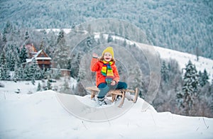 Cute boy enjoying a sleigh ride. Child sledding, riding a sledge play outdoors in snow in winter park.