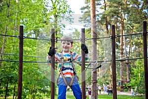 Cute boy enjoying a sunny day in a climbing adventure activity park. shadows from a rope