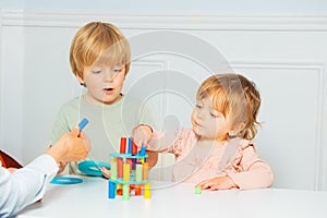 Cute boy and girl build with help of adult tower on the table photo