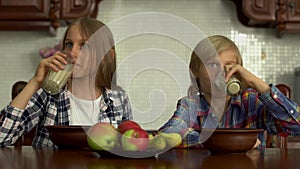 Cute boy and girl drinking milk from glasses. Siblings enjoy their healthy beverage sitting at the table in the kitchen