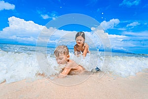 Cute boy and girl having fun on the sunny tropical beach. Lying on sand, wonderful waves around them. View from above.