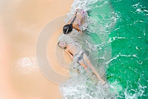 Cute boy and girl having fun on the sunny tropical beach. Lying on sand, wonderful waves around them. View from above.