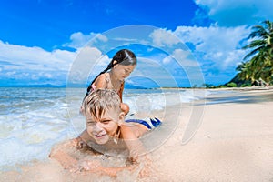 Cute boy and girl having fun on the sunny tropical beach. Lying on sand, wonderful waves around them. View from above.