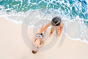 Cute boy and girl having fun on the sunny tropical beach. Lying on sand, wonderful waves around them. View from above.