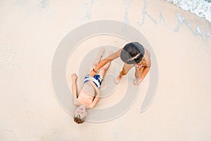 Cute boy and girl having fun on the sunny tropical beach. Lying on sand, wonderful waves around them. View from above.