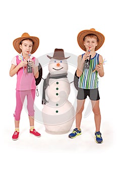 Cute boy and girl holding a cola bottle near a snowman with scarf and hat
