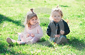 Cute boy and girl sit on grass on summer field. Baby child in green grass on spring lawn. Little kids walking in the