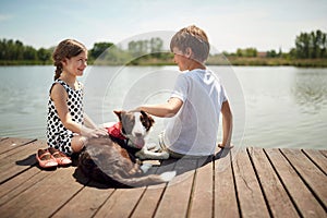 Cute boy and girl sitting by the river, smiling, talking, cuddling the dog