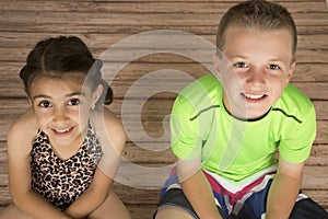 Cute boy and girl sitting on wood floor looking up