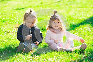 Cute boy and girl on summer field. Happy children playing sitting on green grass in spring park.