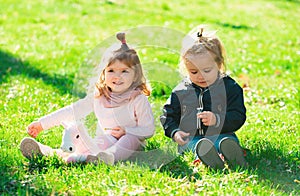 Cute boy and girl on summer field. Happy children playing sitting on green grass in spring park.