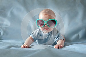 Cute boy in green sunglasses lying on a blue background and smiling