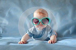 Cute boy in green sunglasses lying on a blue background and smiling