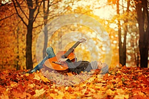 Cute boy with guitar, lying on the grass in autumn sunny day