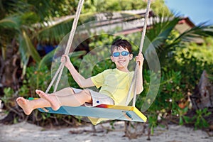 Cute boy having fun swinging at tropical island beach