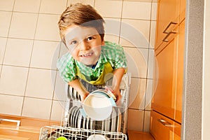 Cute boy holding bowls standing next to dishwasher photo