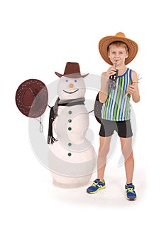 Cute boy holding a cola bottle near a snowman with scarf and hat