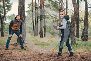cute boy holding rugby ball and smiling at camera while playing football with father