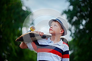 Cute boy holding skateboard in hand outdoors.Wearing cap and stylish clothes