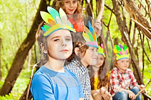 Cute boy in Injun`s headdress playing with friends