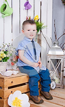 Cute boy in jeans suit sitting on a bright background juicy