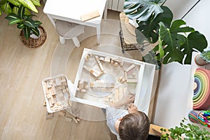 Cute boy kid playing sensory box kinetic sand table with Montessori wooden materials. Top view.
