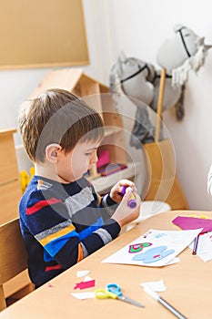 Cute boy on kindergarten art class gluing colorful paper