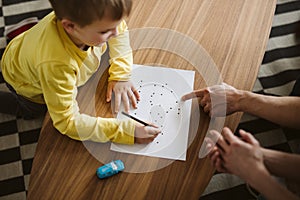 Cute boy kneeling on the floor and connecting dots on a piece of paper photo